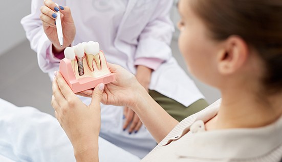 Woman holding sample dental implant during consultation with dentist
