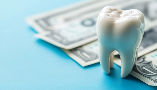 Large model tooth on blue surface next to dollar bills