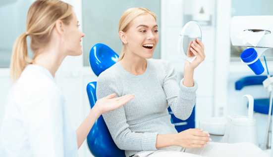 Woman in dental chair smiling at results in mirror