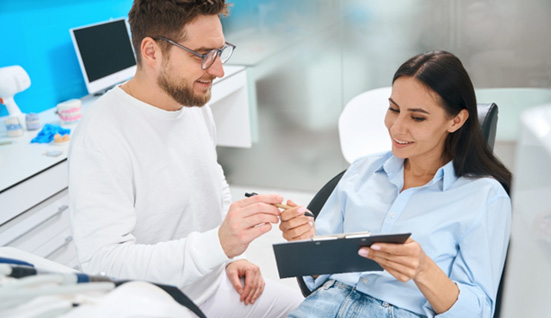 Dentist in white handing forms to patient to fill out