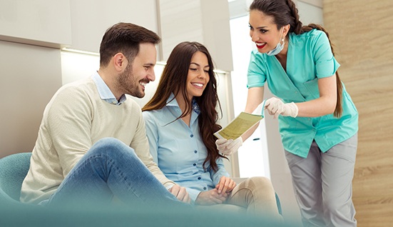 Couple smiling while reviewing paperwork with dental assistant