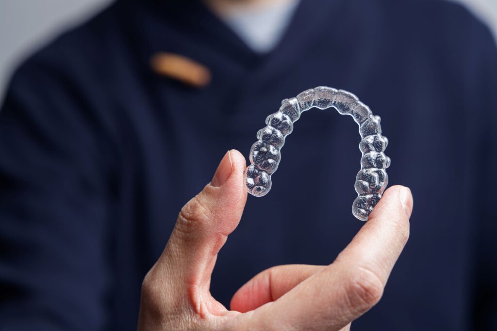 Closeup of man in dark blue scrubs holding single Invisalign tray
