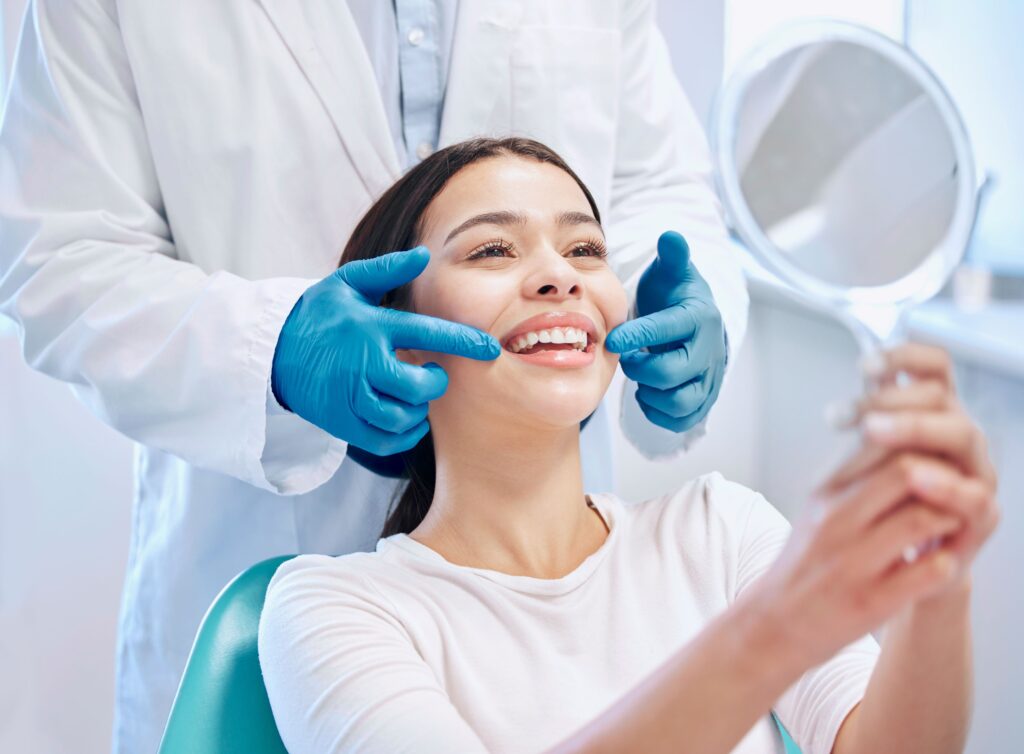 Dentist in blue gloves touching patient's cheeks as she smiles into mirror